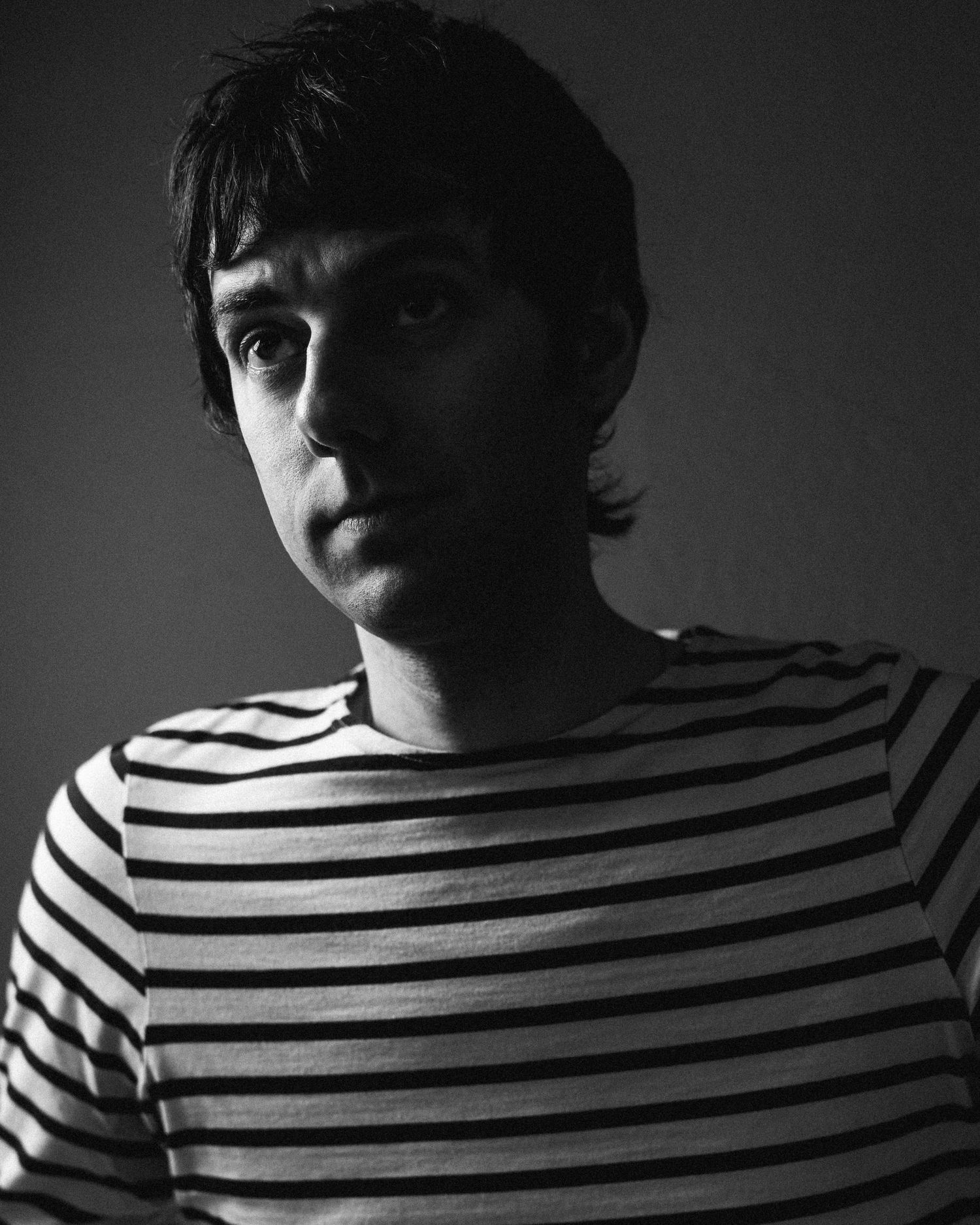 A dramatic black and white sequence showing a person in a striped shirt shifting position in shadowy lighting.