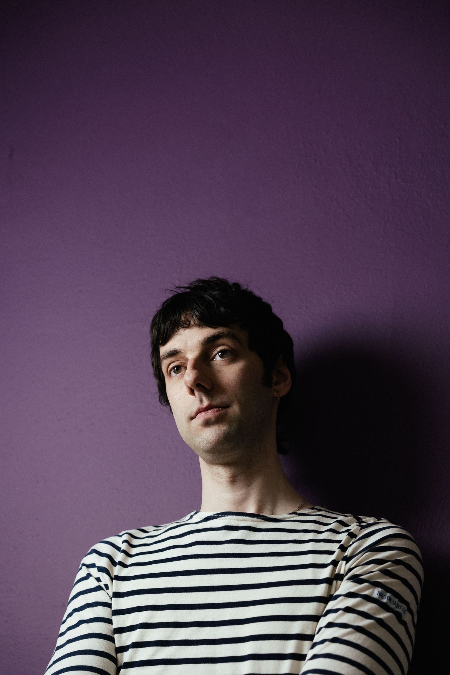 Portrait against purple wall showing person in black and white striped shirt looking upward with dramatic lighting.