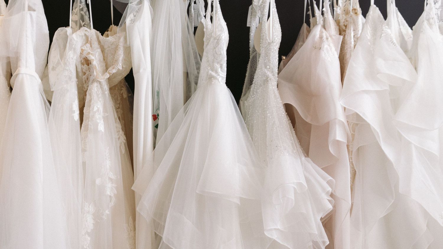 A collection of white wedding dresses hanging in a row at a bridal boutique shop.