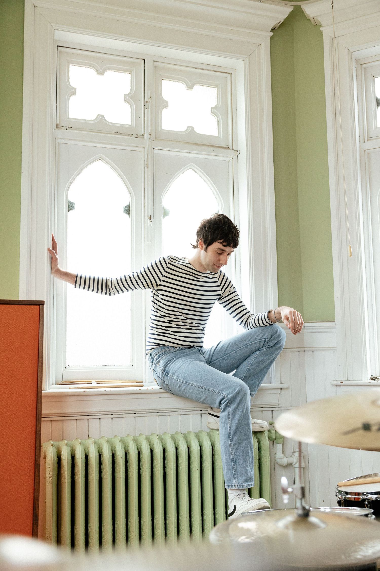 A person in striped shirt and jeans performs a sequence of parkour-style jumps near a window and radiator.