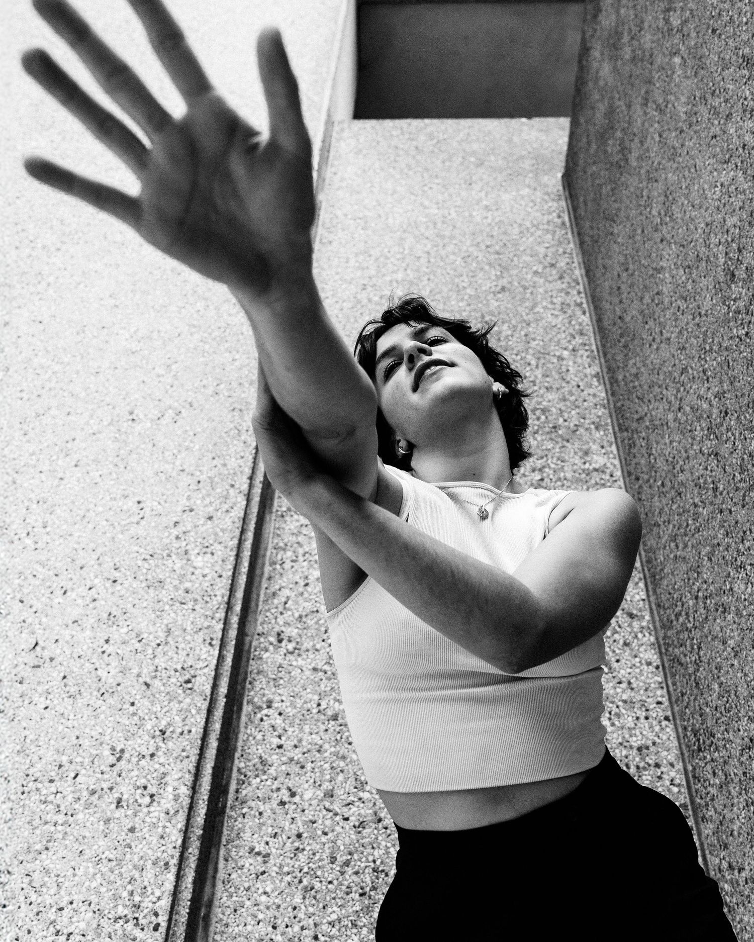 Black and white artistic photograph showing a dramatic upward reaching pose against a geometric architectural background.