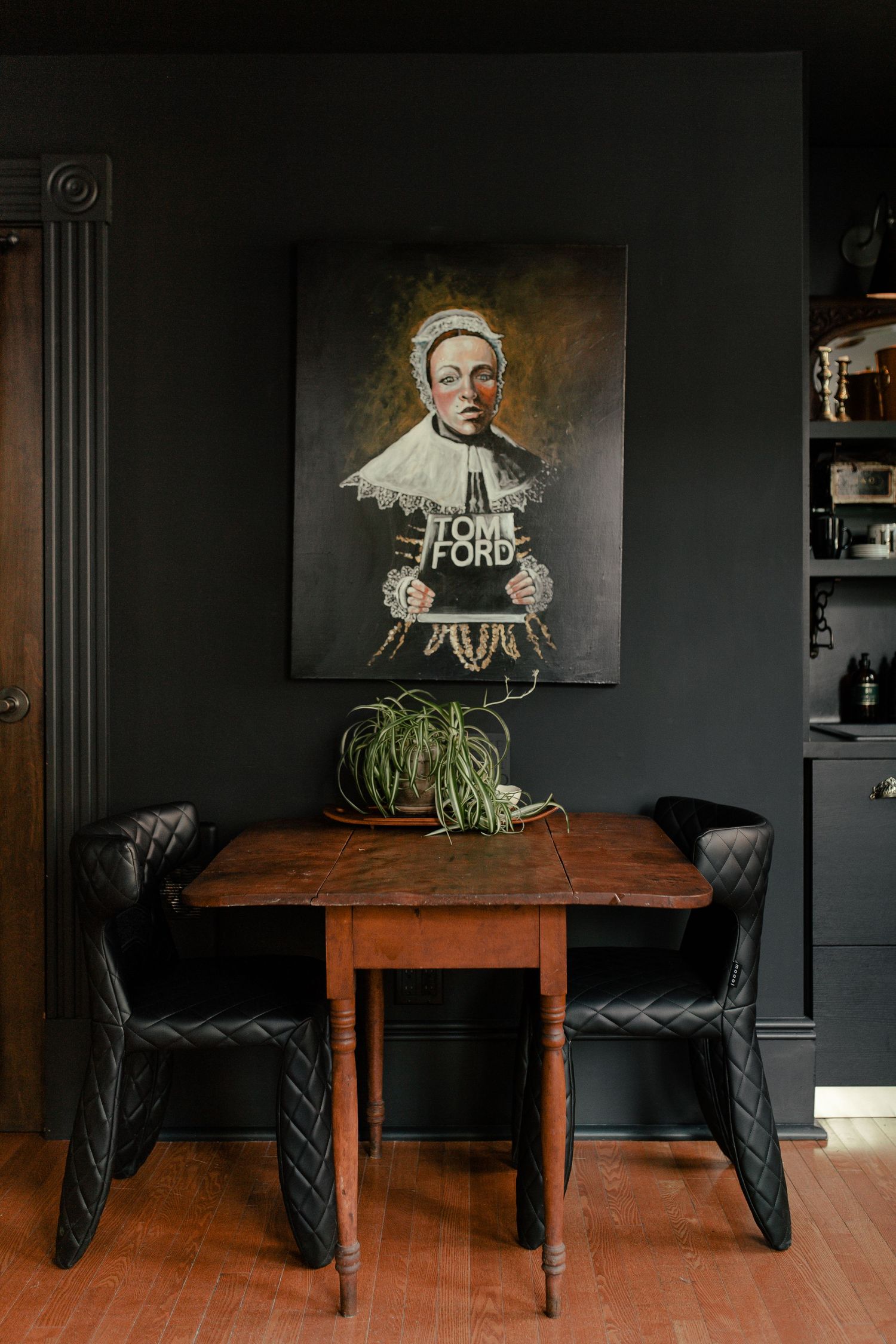 Small dining nook with rustic wooden table, black chairs, and vintage portrait artwork on dark grey wall.