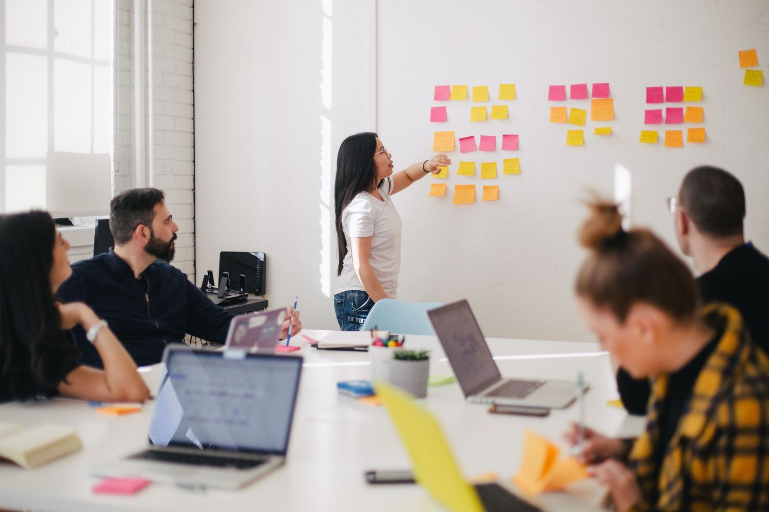 Team members collaborate at a long conference table with laptops and colorful sticky notes posted on the wall during a workshop.