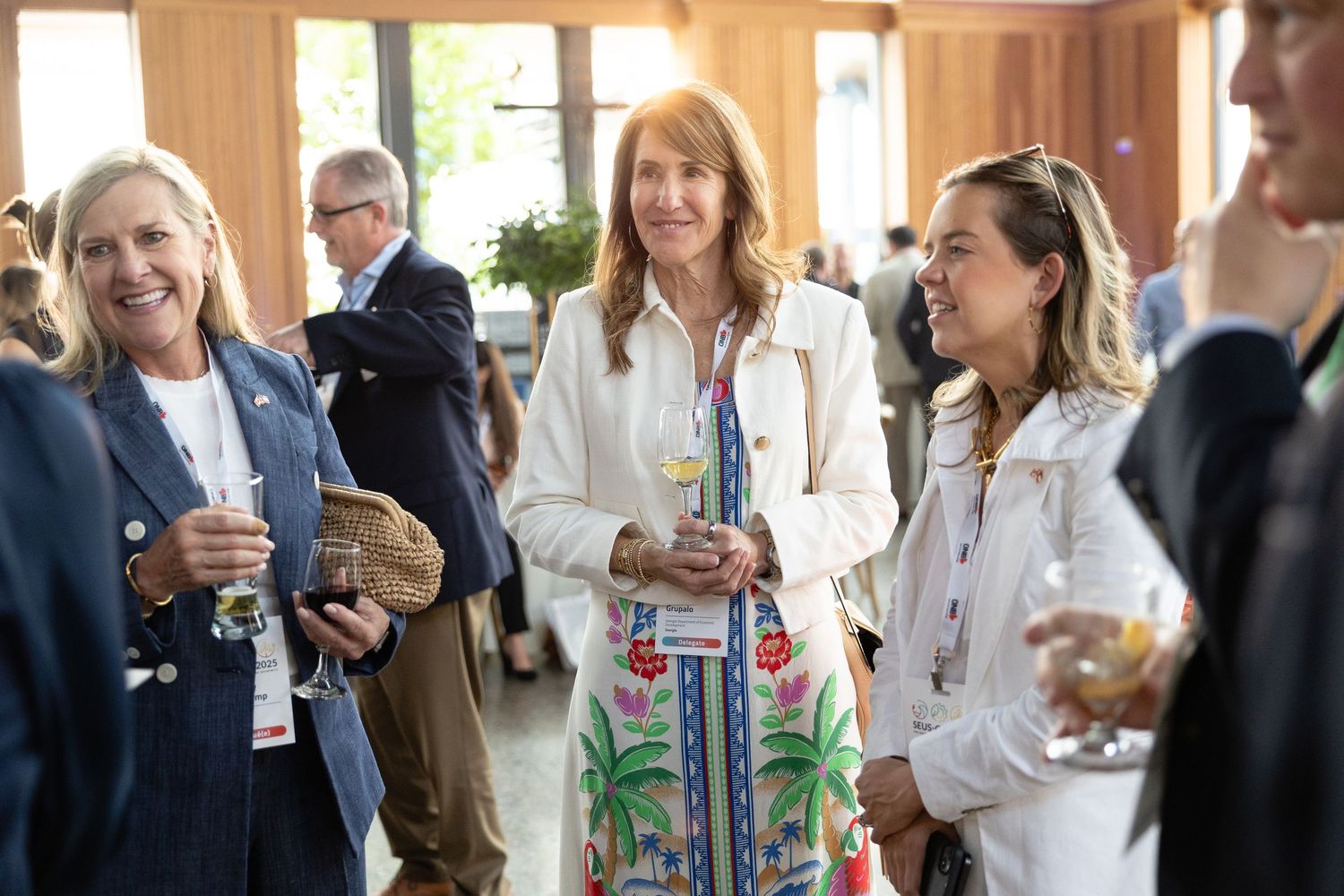 A group of professionals in business attire networking and socializing at an indoor event with beverages.