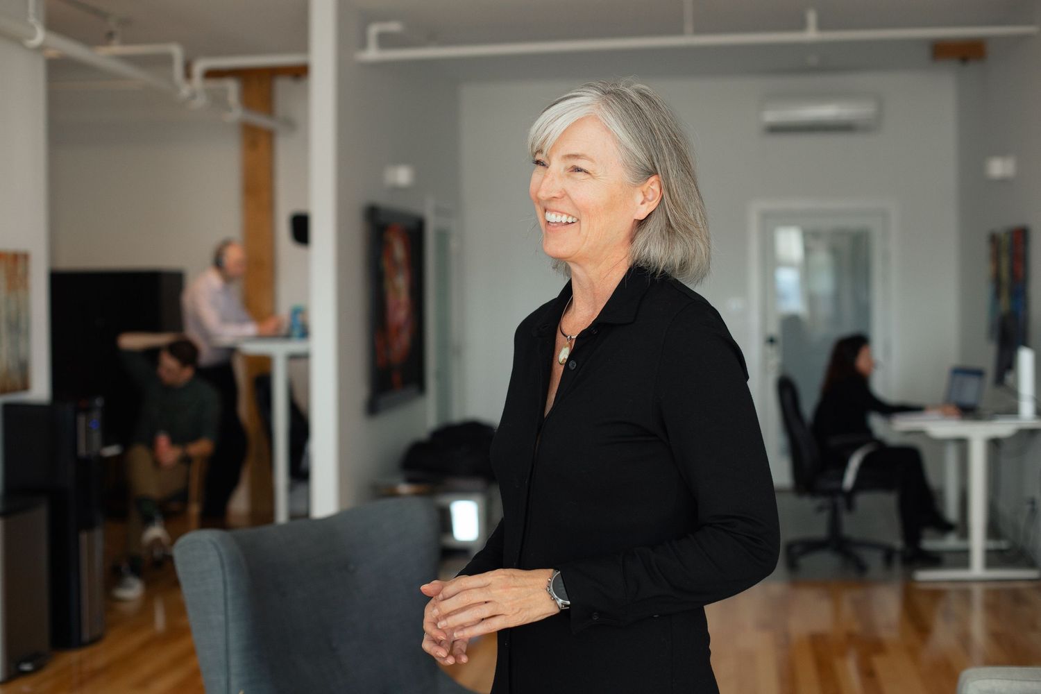 Professional woman in black attire laughing joyfully in a modern office setting.