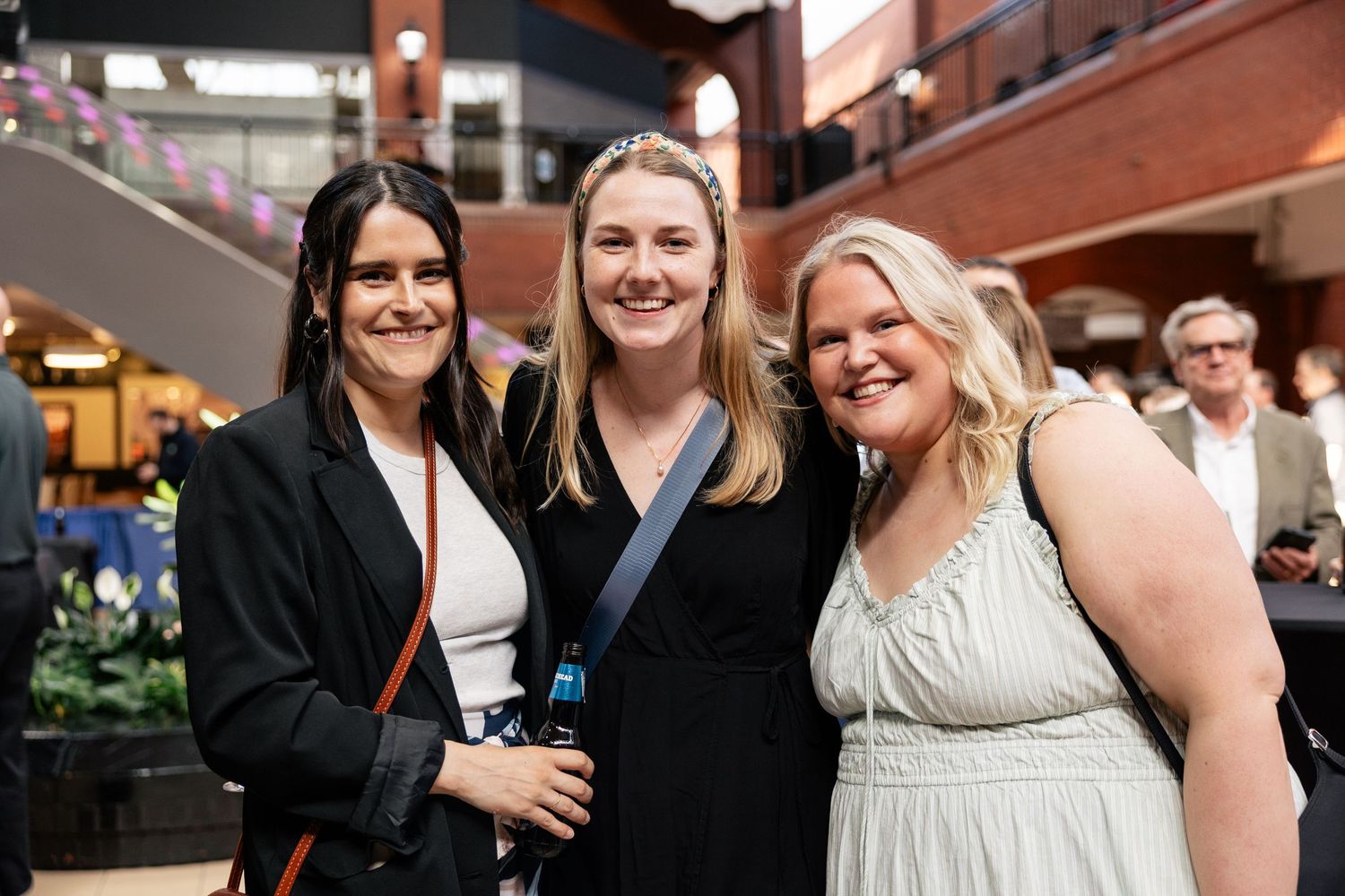 Three attendees smiling together at an indoor event venue with brick walls and ambient lighting.