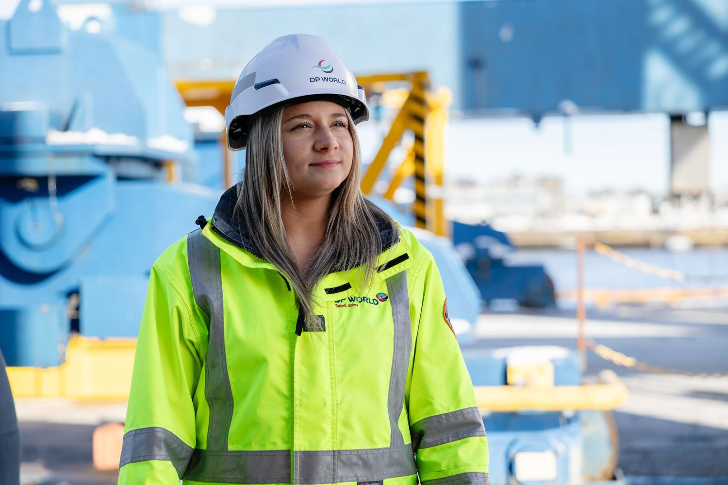 A construction worker wearing a safety helmet and high-visibility yellow jacket stands at an industrial worksite.