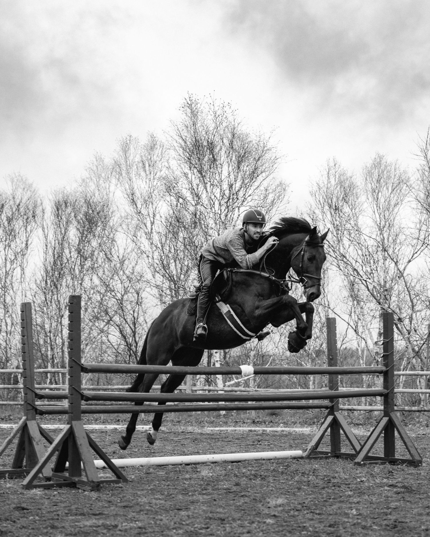 Black and white photograph of an equestrian and horse jumping over a fence during a training session.