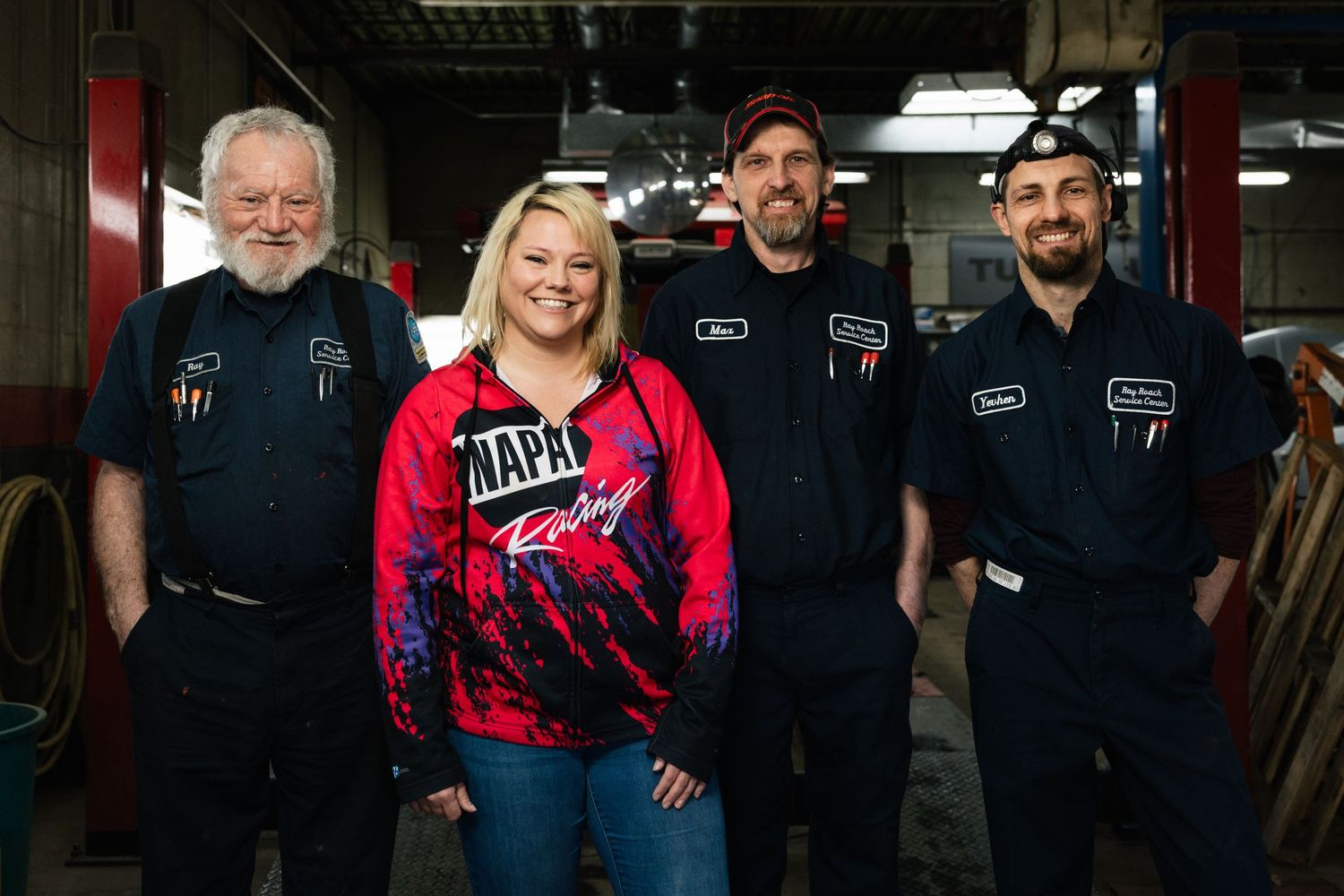People in dark uniforms and casual clothing posing together in what appears to be a workshop or garage setting.