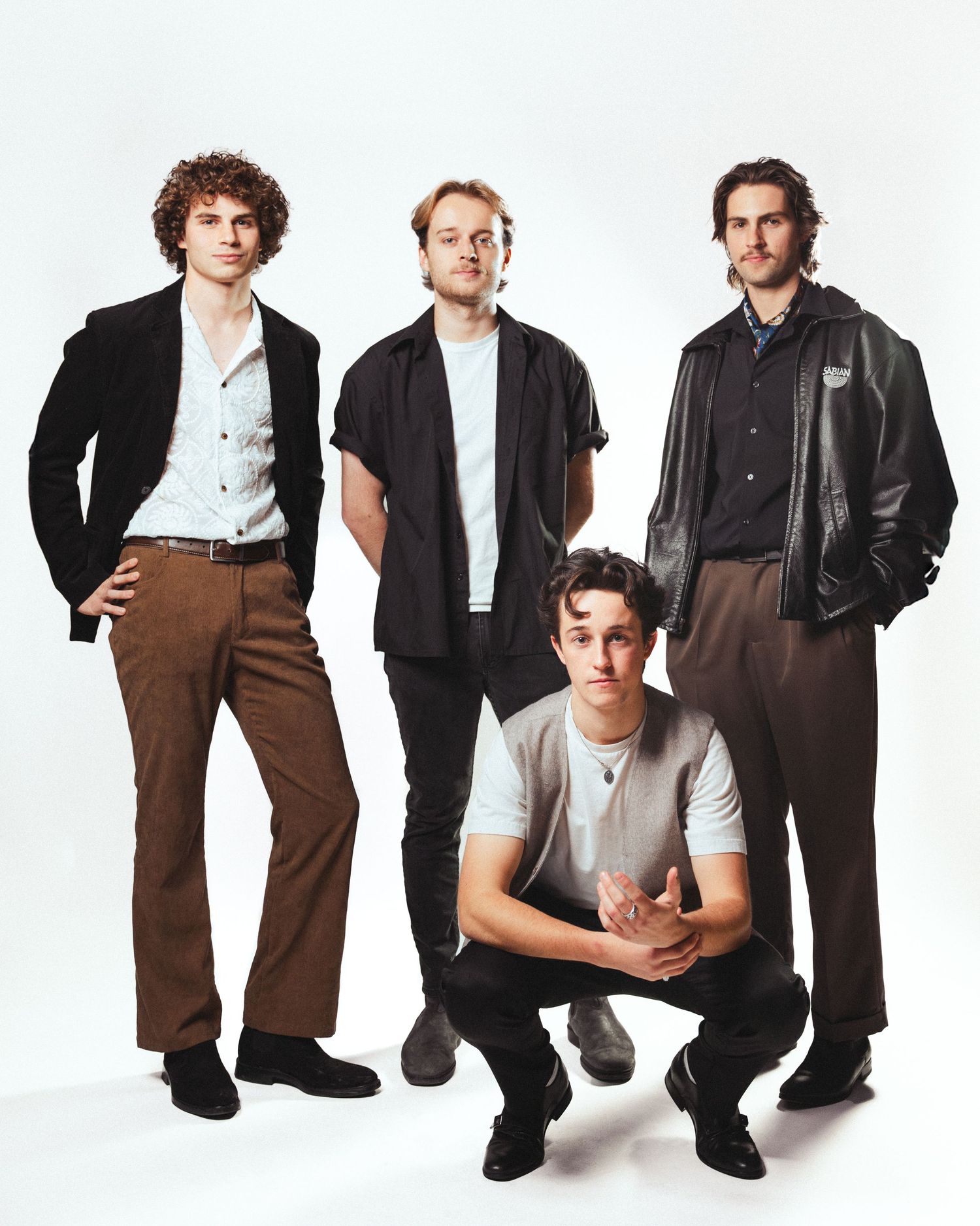 Four men in casual and semi-formal attire pose together in a white studio, showcasing modern masculine fashion styles.