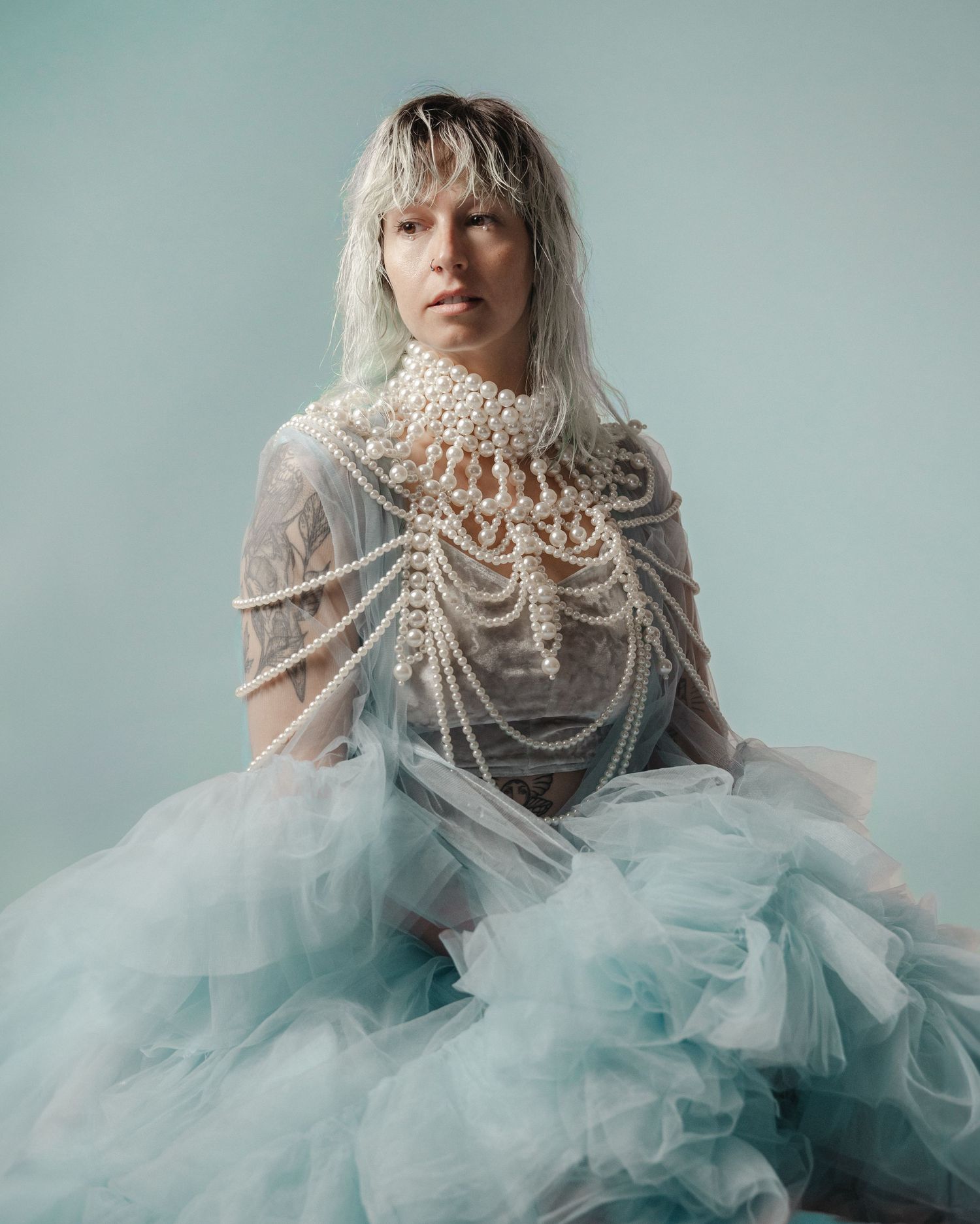 A stunning fashion portrait featuring ethereal pearls and layers of airy turquoise tulle against a soft blue backdrop.