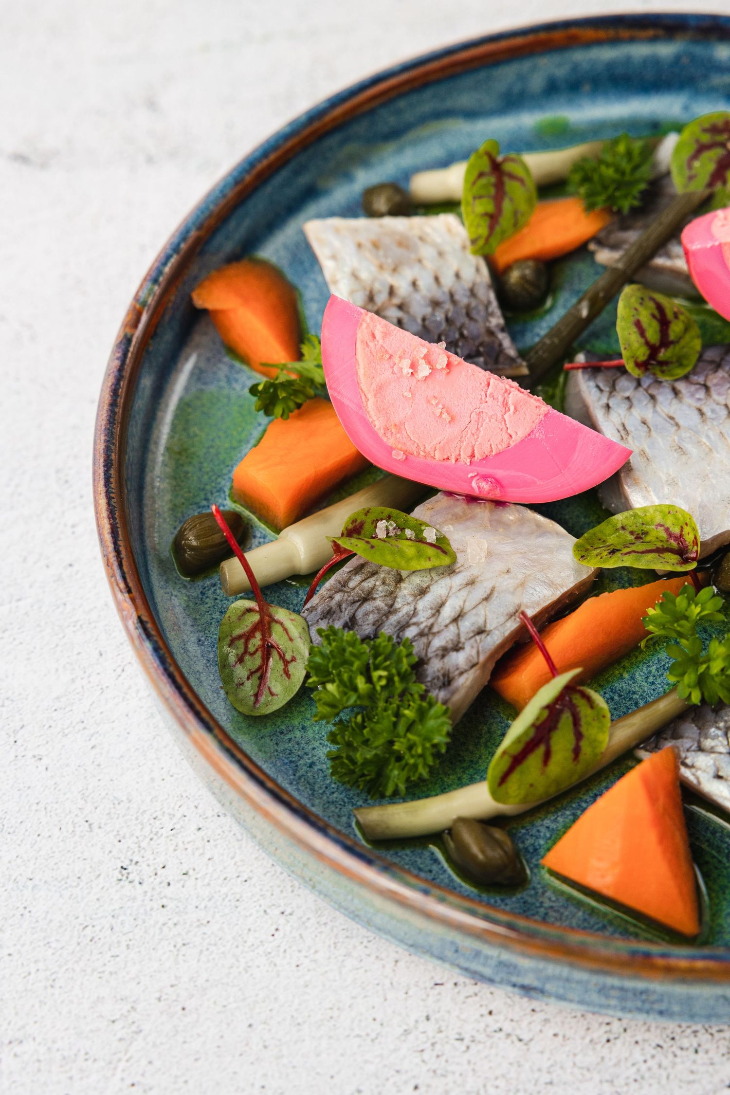 Sliced colorful vegetables and pink pickled eggs arranged on a rustic blue ceramic plate with fresh herbs.
