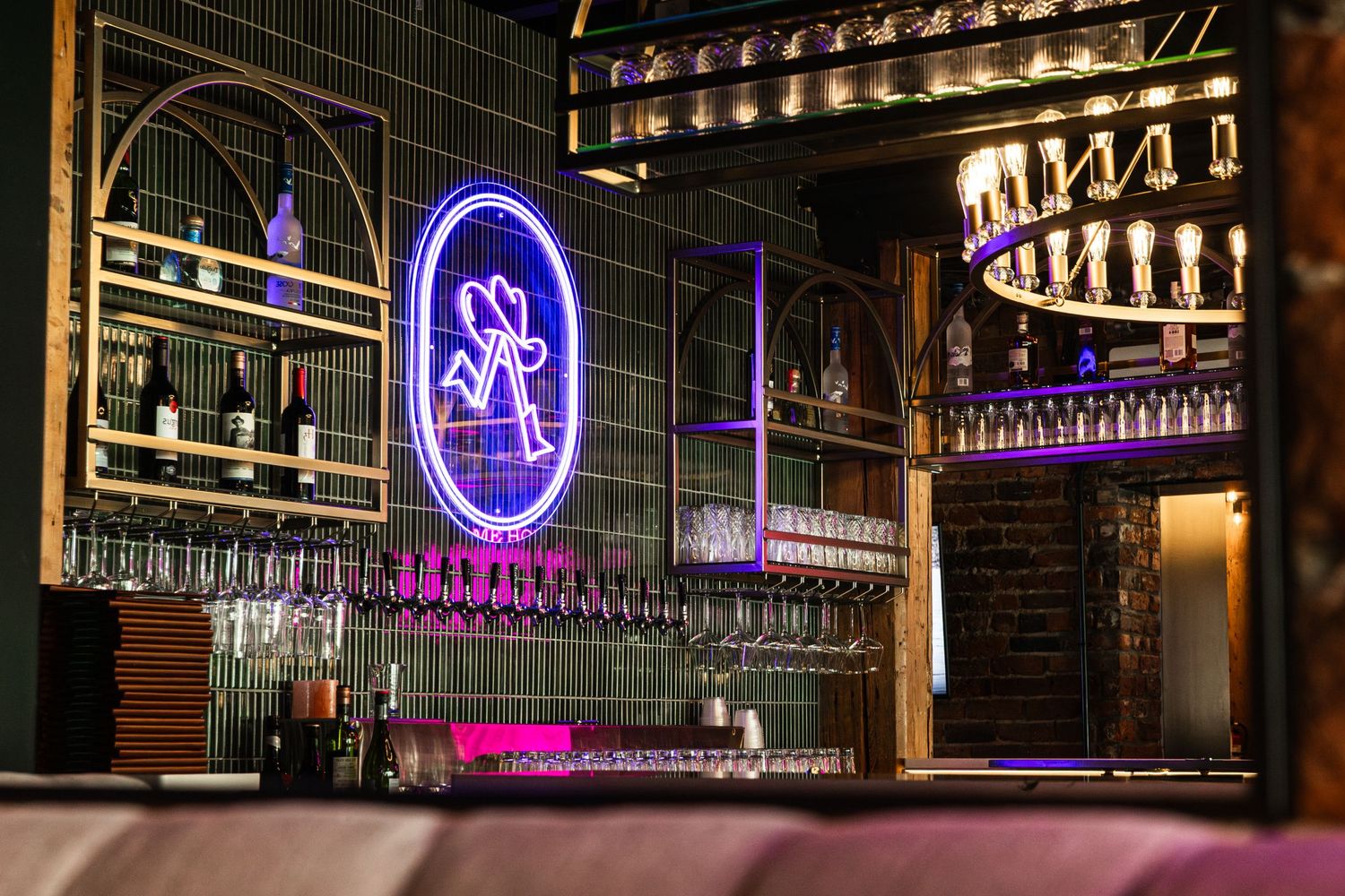 Illuminated purple neon signage glows above a modern bar display with glass shelving and bottles at night.