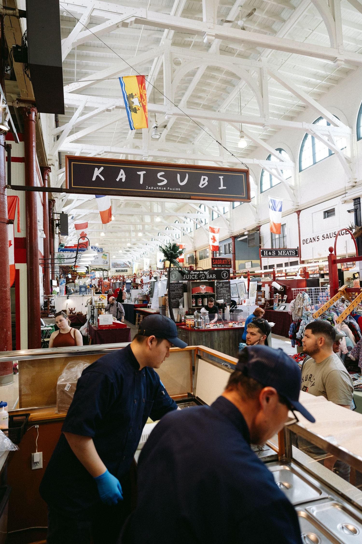 Bustling scene inside a busy market hall with Katsubi restaurant signage and international flags hanging from the ceiling.