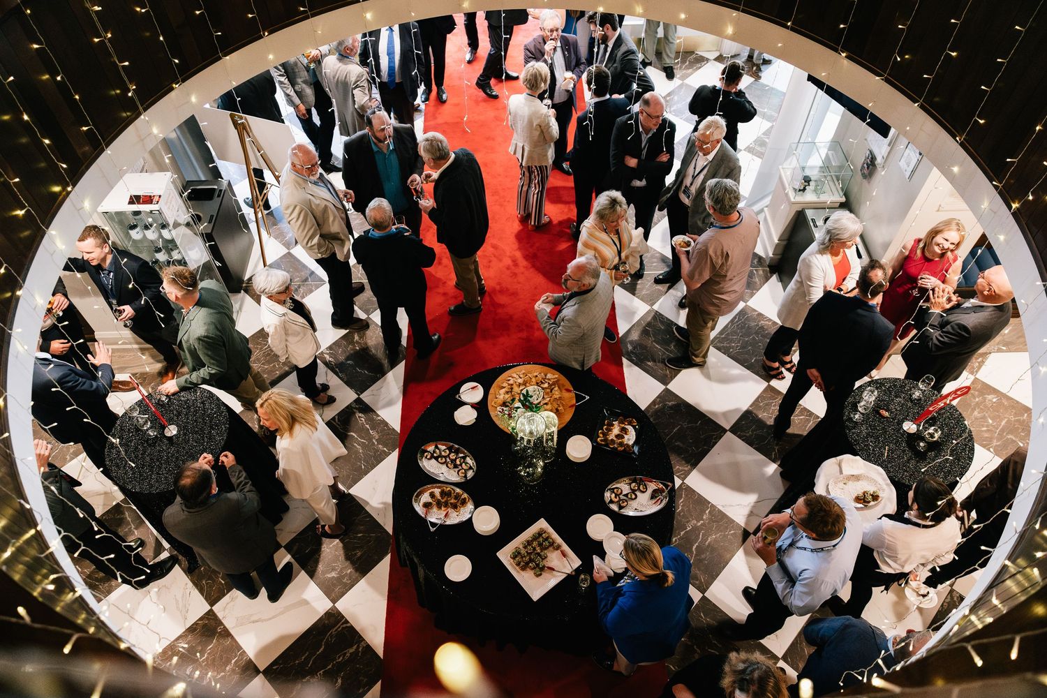 Aerial view of an elegant wedding reception with guests mingling on a black and white checkered floor with red carpet.