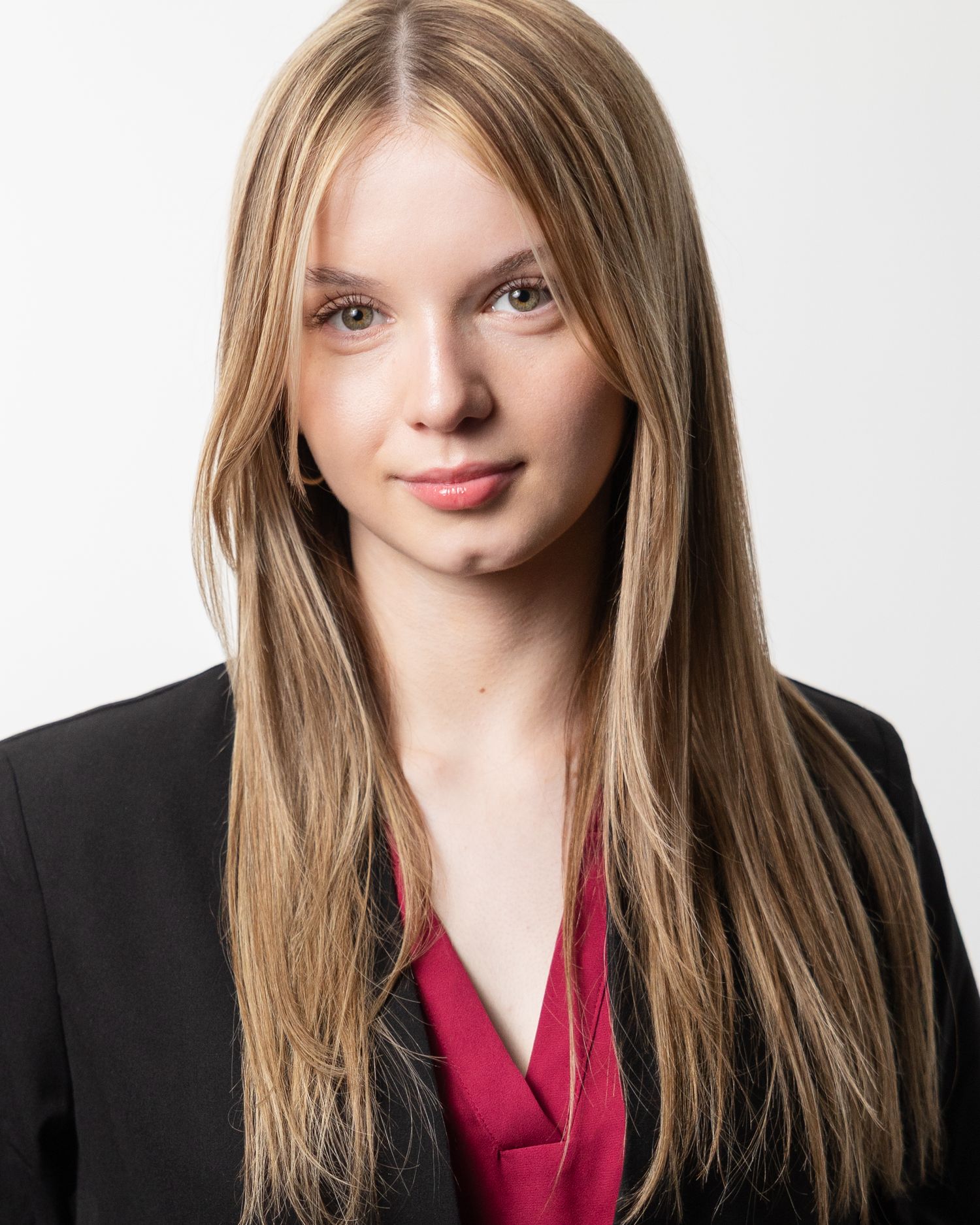 Professional headshot of someone wearing a black blazer and red blouse against a white background.