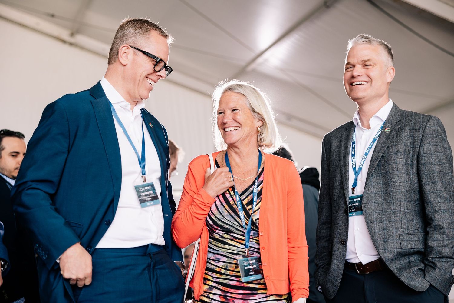 Three business professionals sharing a laugh during a conference, one wearing an orange blazer.