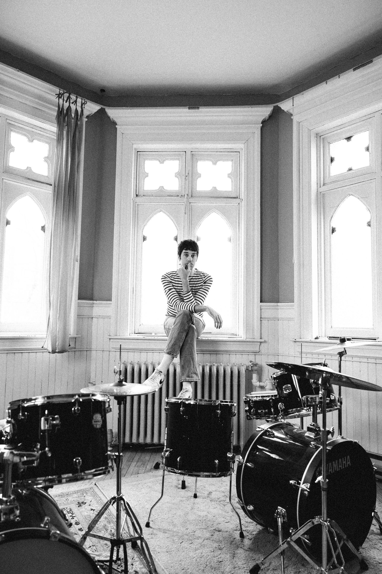 A monochromatic series of drum kits set up in a bright room with gothic-style windows and white trim molding.