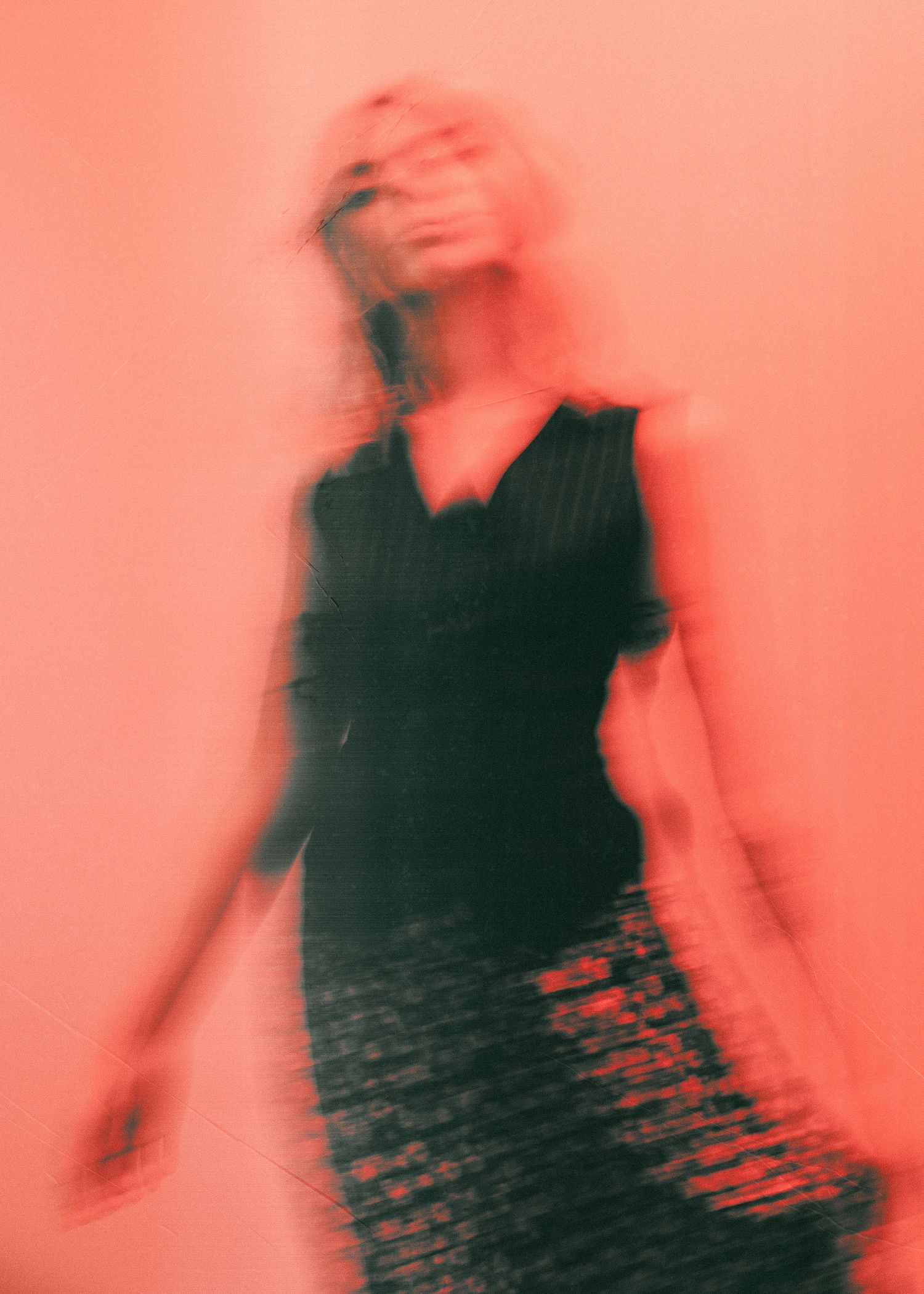 Artistic blurred motion portrait in black against coral pink background creating ethereal dreamy effect.