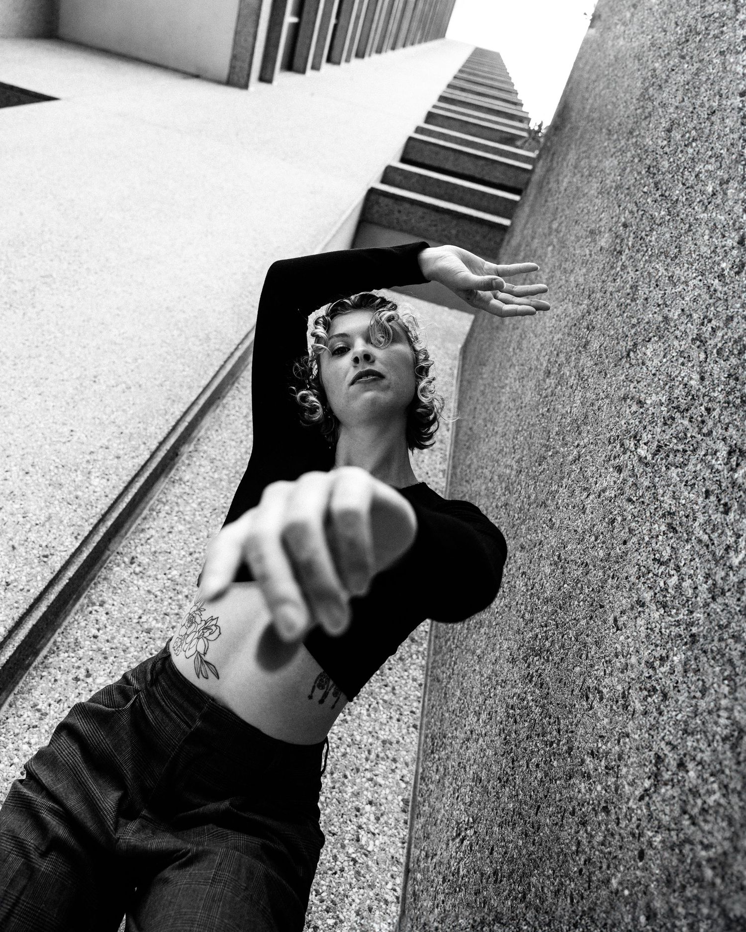 Black and white artistic photograph from low angle perspective showing a figure posed against a wall with extended arms.