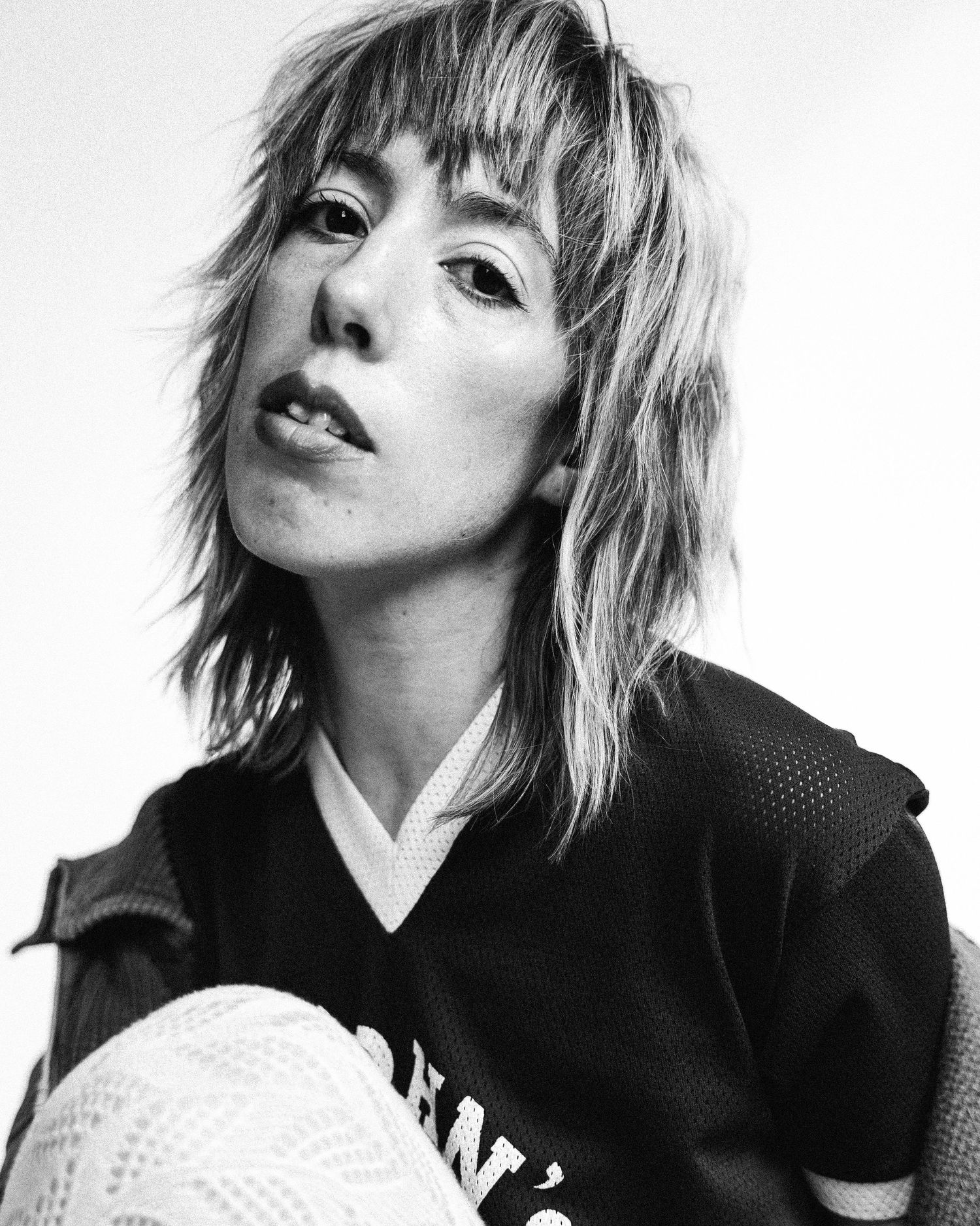 Black and white artistic portrait in moody lighting showing shaggy layered hair and intense expression against dark background.