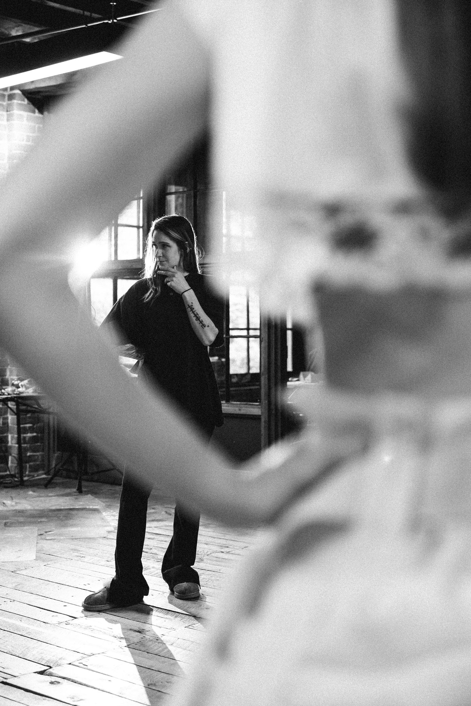 Black and white artistic photo showing dance studio rehearsal with blurred foreground elements and architectural details.