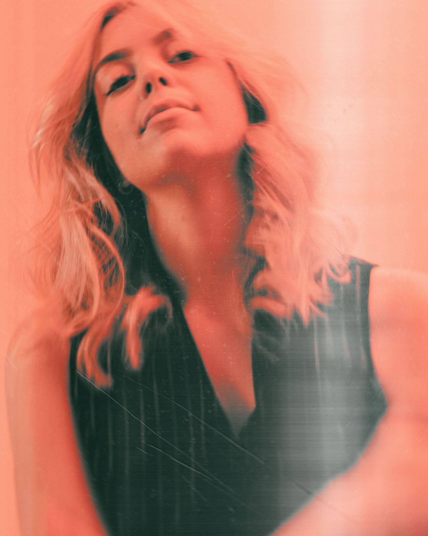Artistic portrait with dreamy coral-tinted lighting showing upward glancing pose against soft ethereal background.