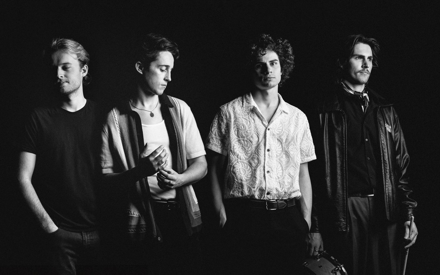 Black and white photograph of a four-member rock band posing against a dark background.