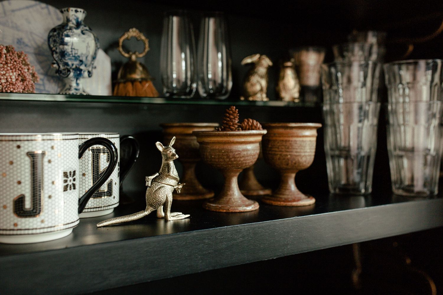 A rustic collection of clay pots, wooden shelves, and kitchen accessories arranged in a vintage-style farmhouse setting.