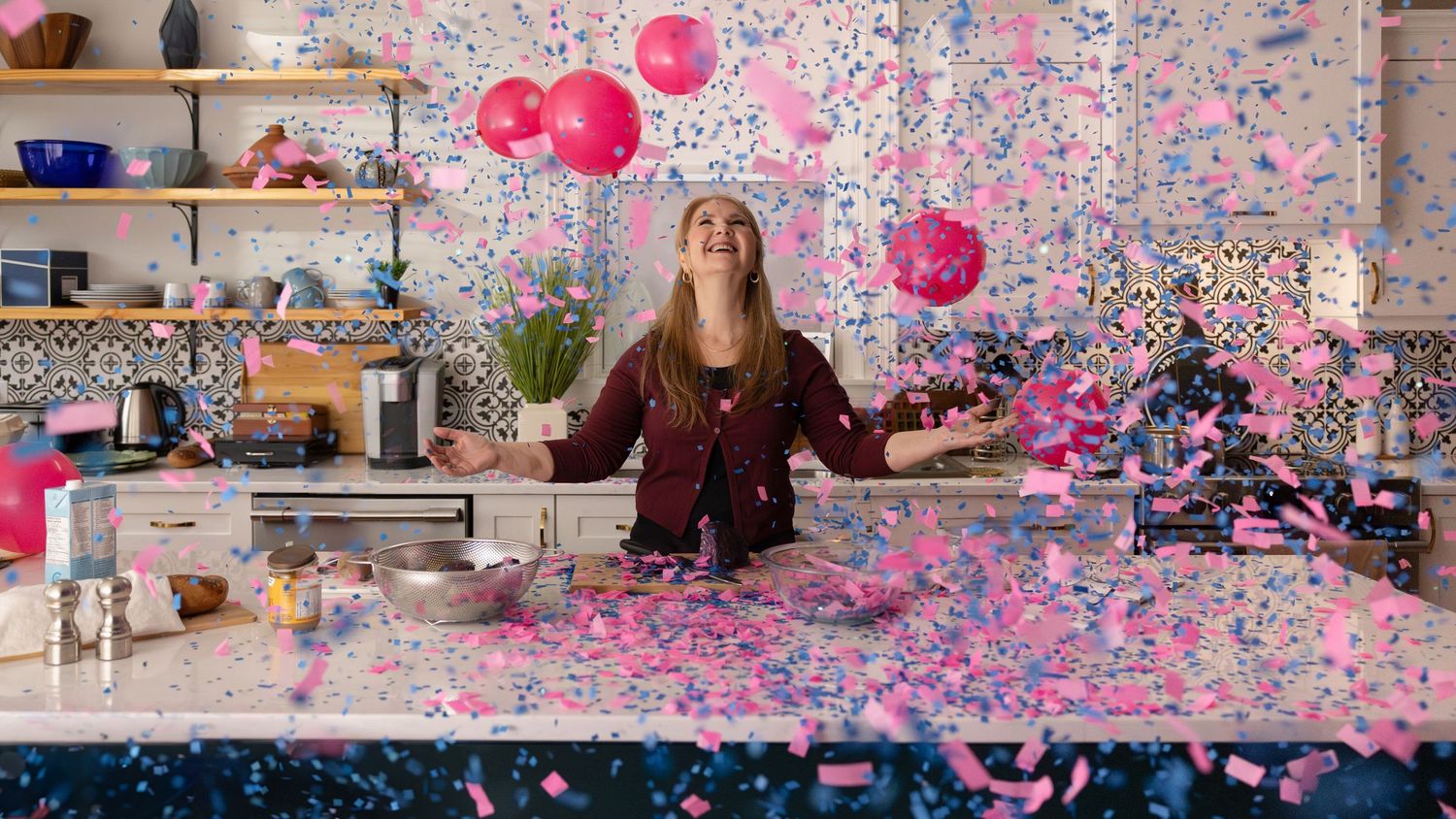 A group of people celebrating with pink and blue confetti falling in a room during a festive party gathering.