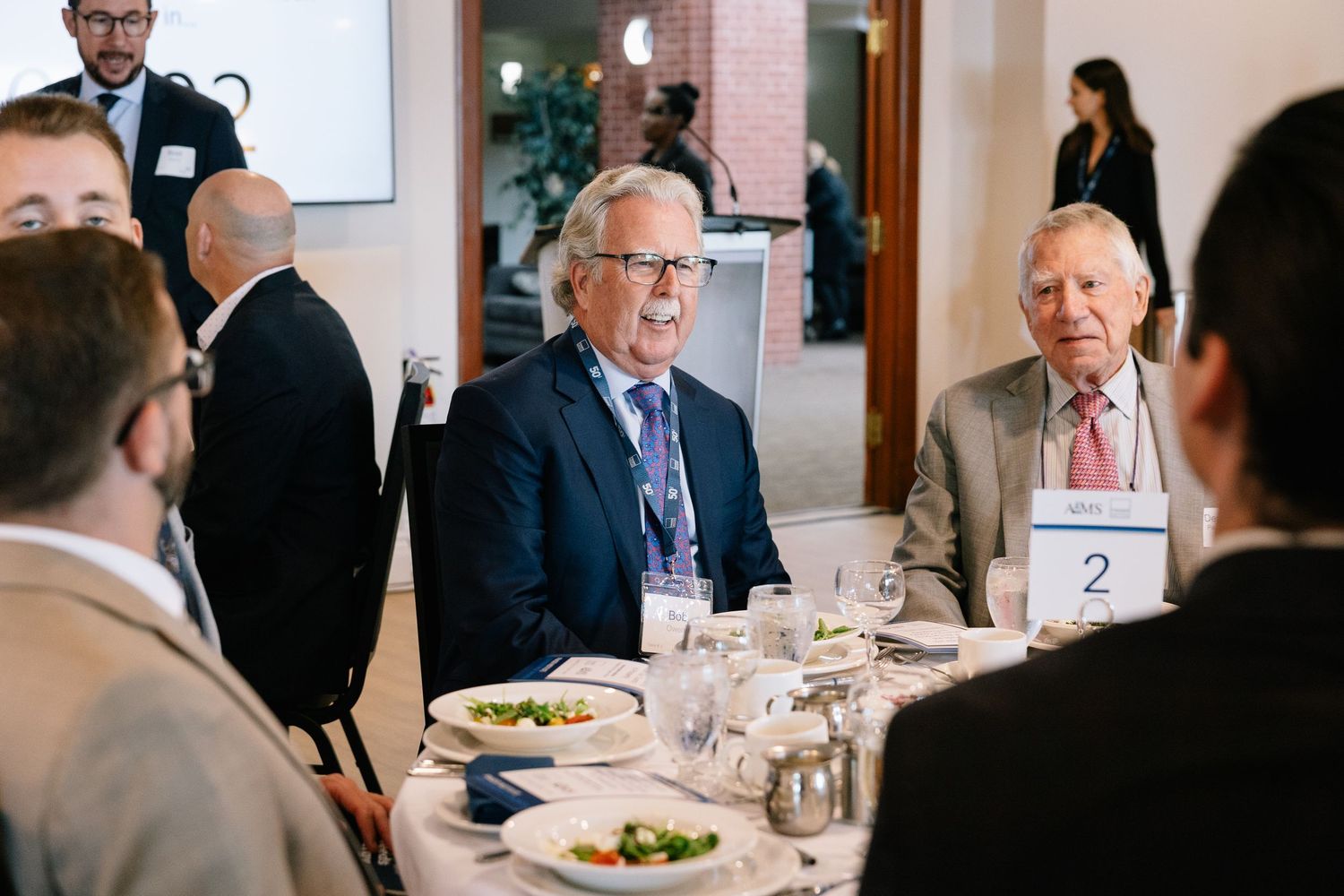 Business professionals engage in conversation during a corporate dining event at a conference table.