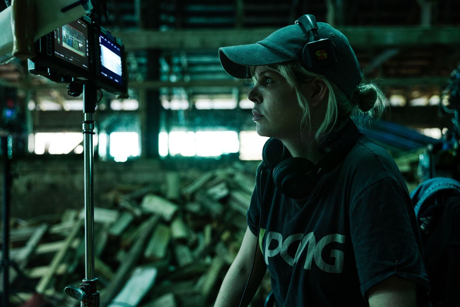Camera operator wearing a baseball cap films in dark moody lighting with green tint atmosphere.