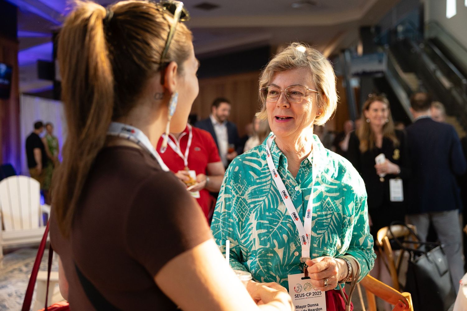 Two people having an engaged conversation at a professional event, with one wearing a vibrant turquoise patterned blouse.