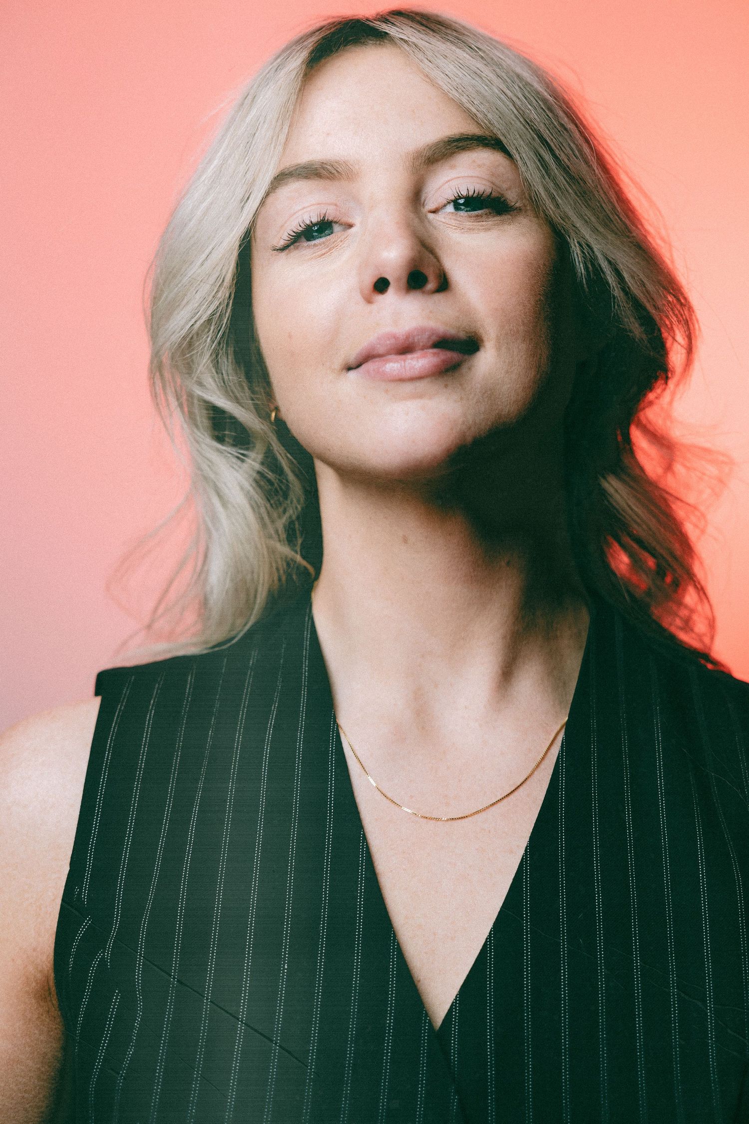 Professional portrait of a person in black pinstripe attire against a pink backdrop.