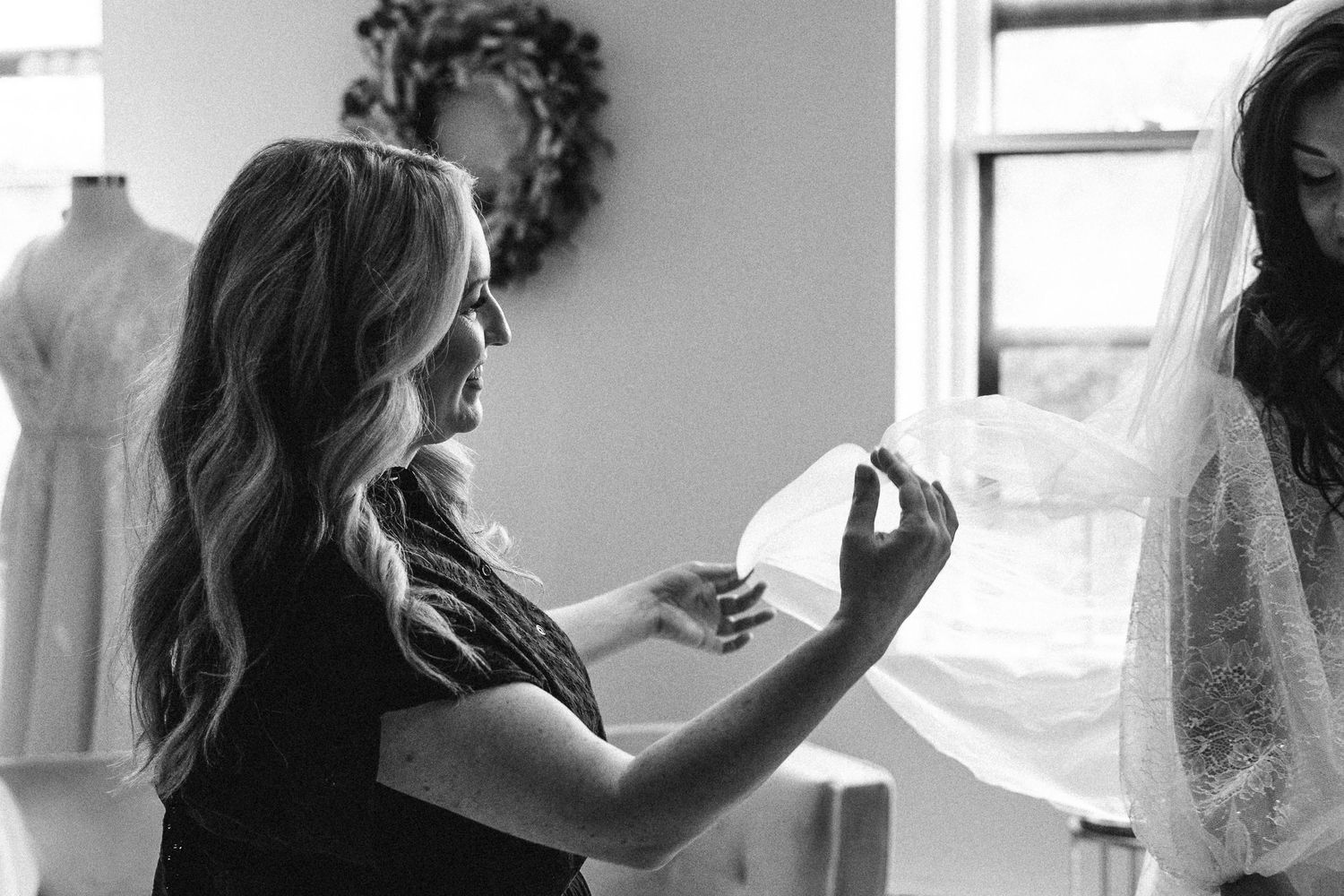 A black and white photograph shows hands adjusting delicate white fabric against a bright window.