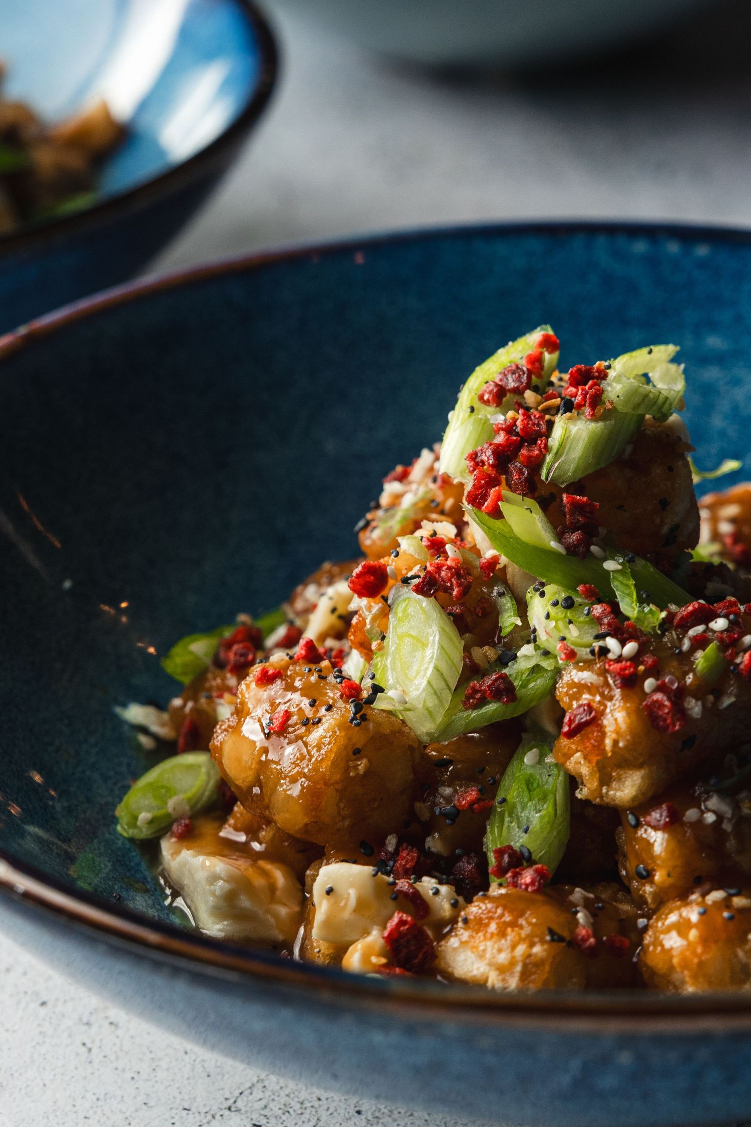 Honey garlic chicken topped with green onions, sesame seeds, and chili flakes served in a blue ceramic bowl.