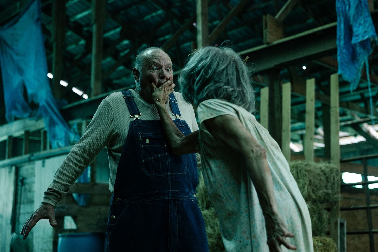 Two figures in a dark, moody horror scene confront each other in a dimly lit industrial setting.