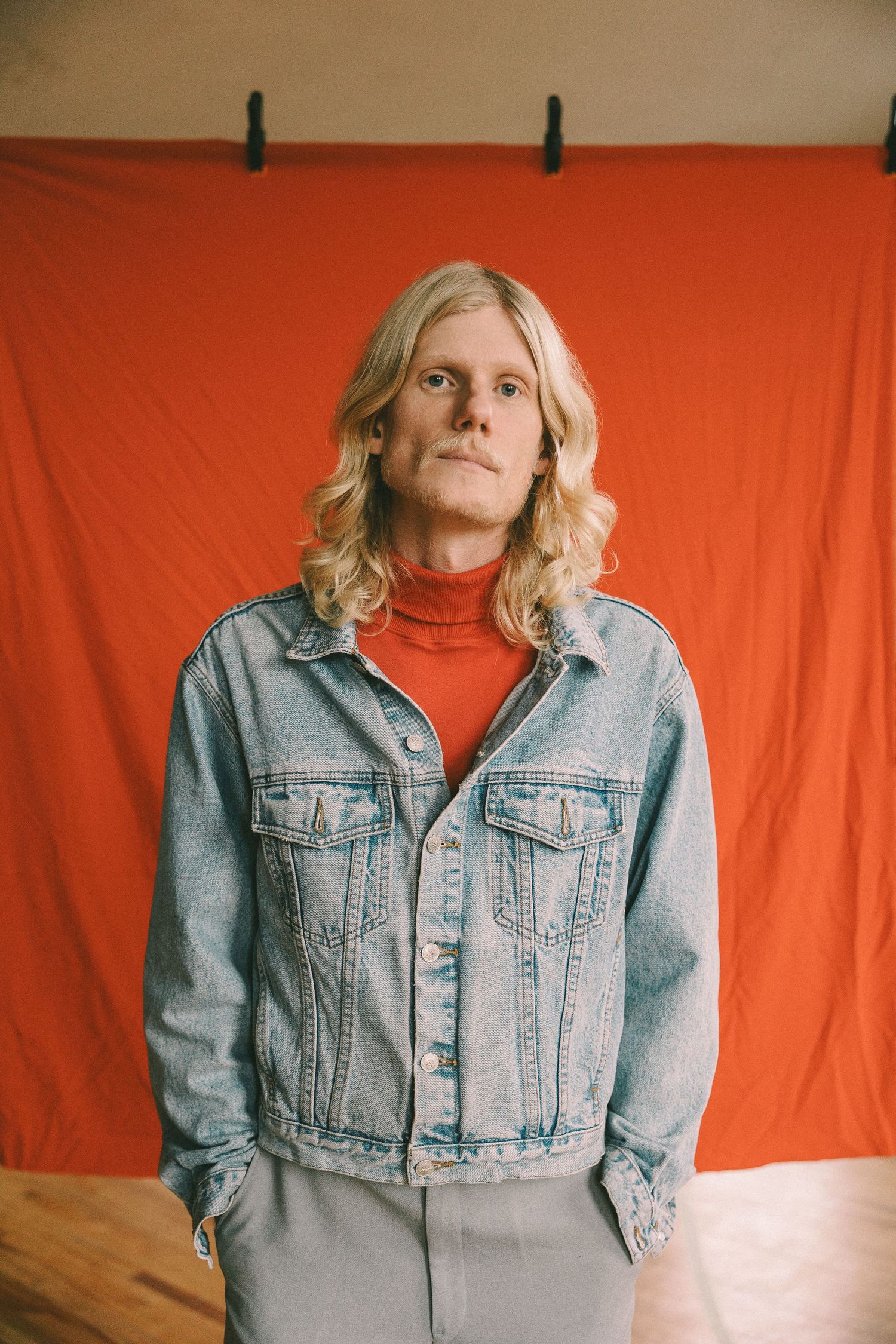 A series of photos against an orange backdrop shows someone wearing a denim jacket and red turtleneck in different poses.