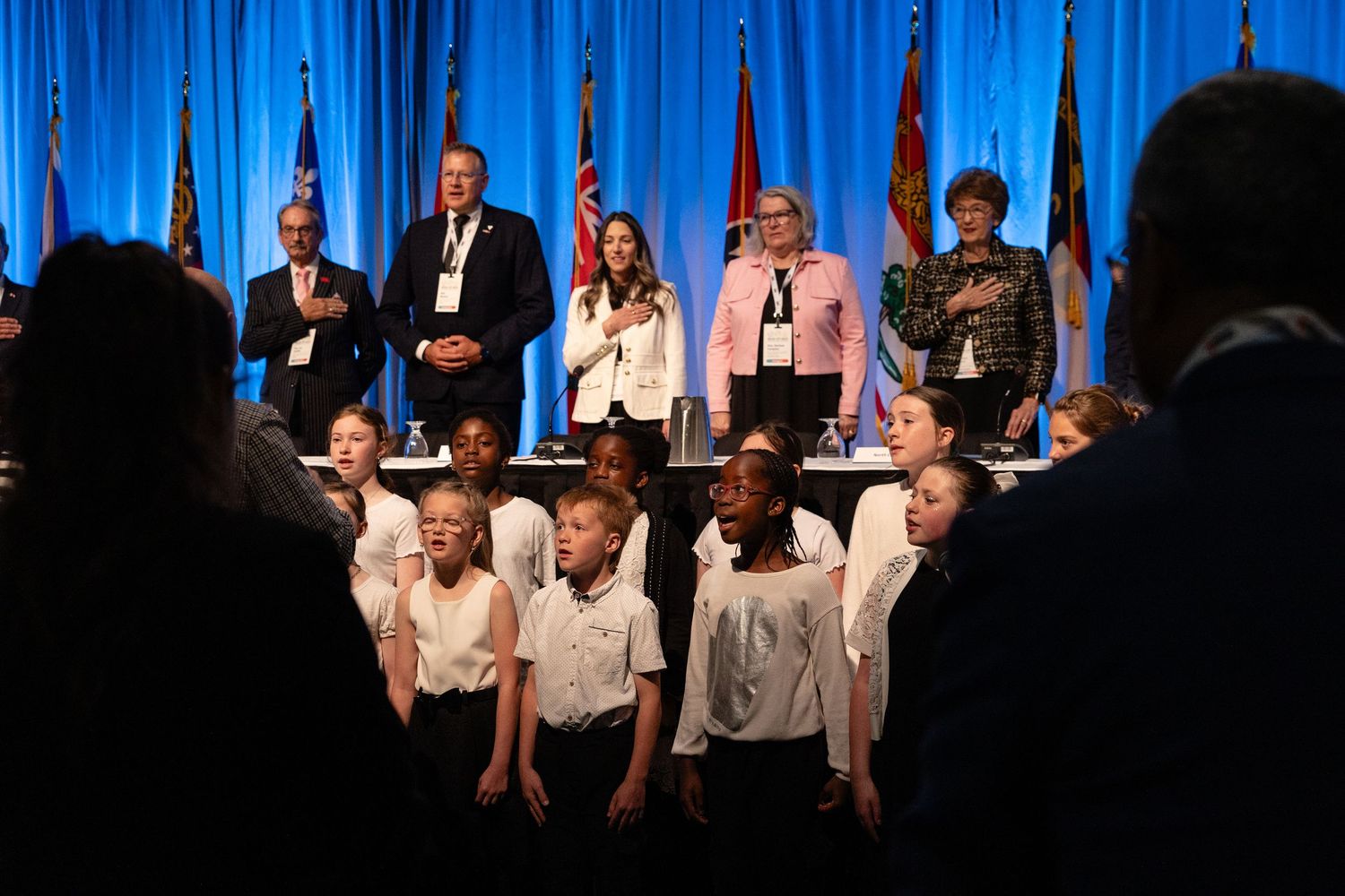 People perform on stage in front of a blue curtain backdrop during a theatrical production.
