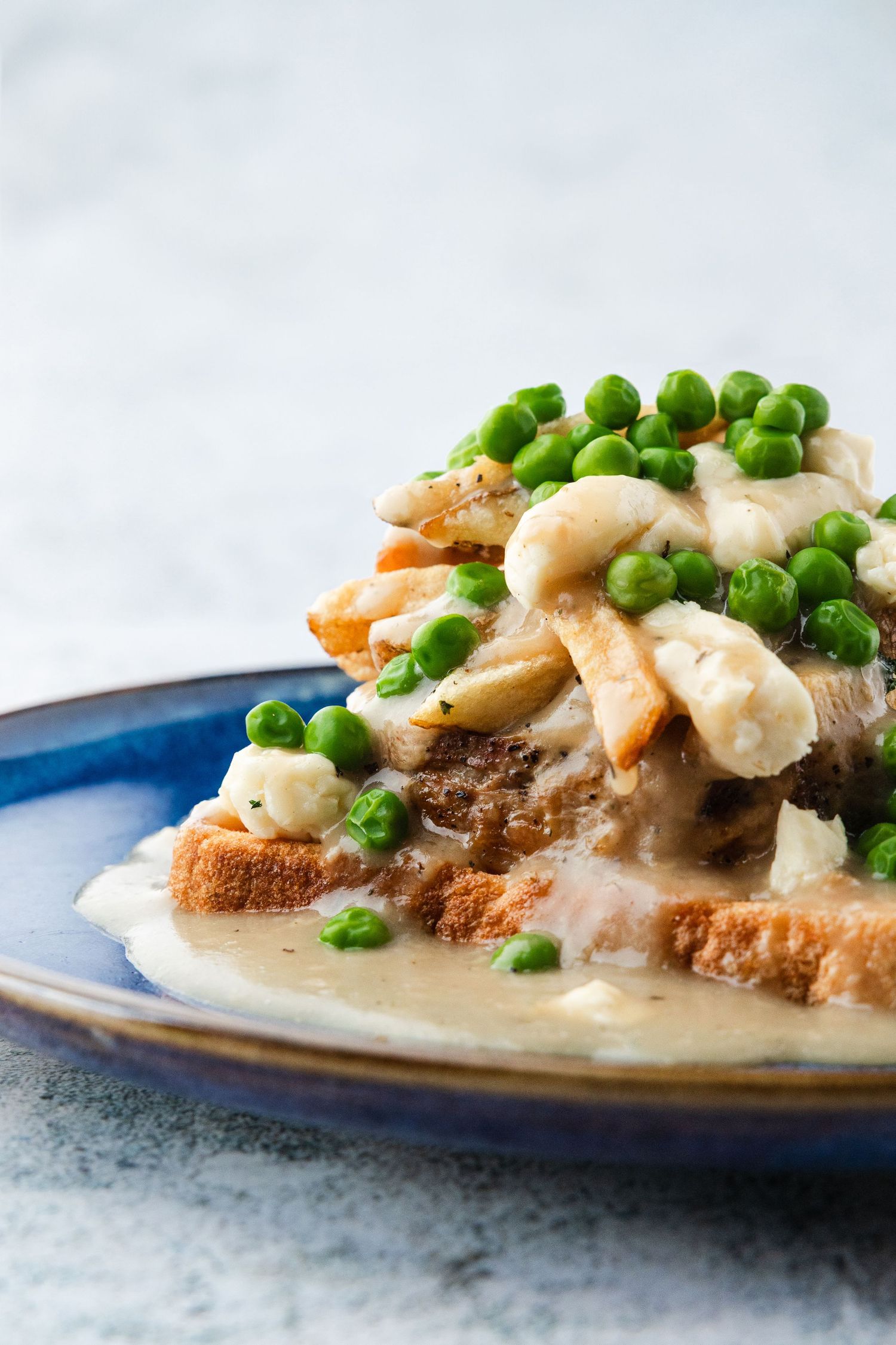 Open-faced sandwich with tender chicken, mushrooms and green peas in creamy sauce served on crusty bread on blue plate.