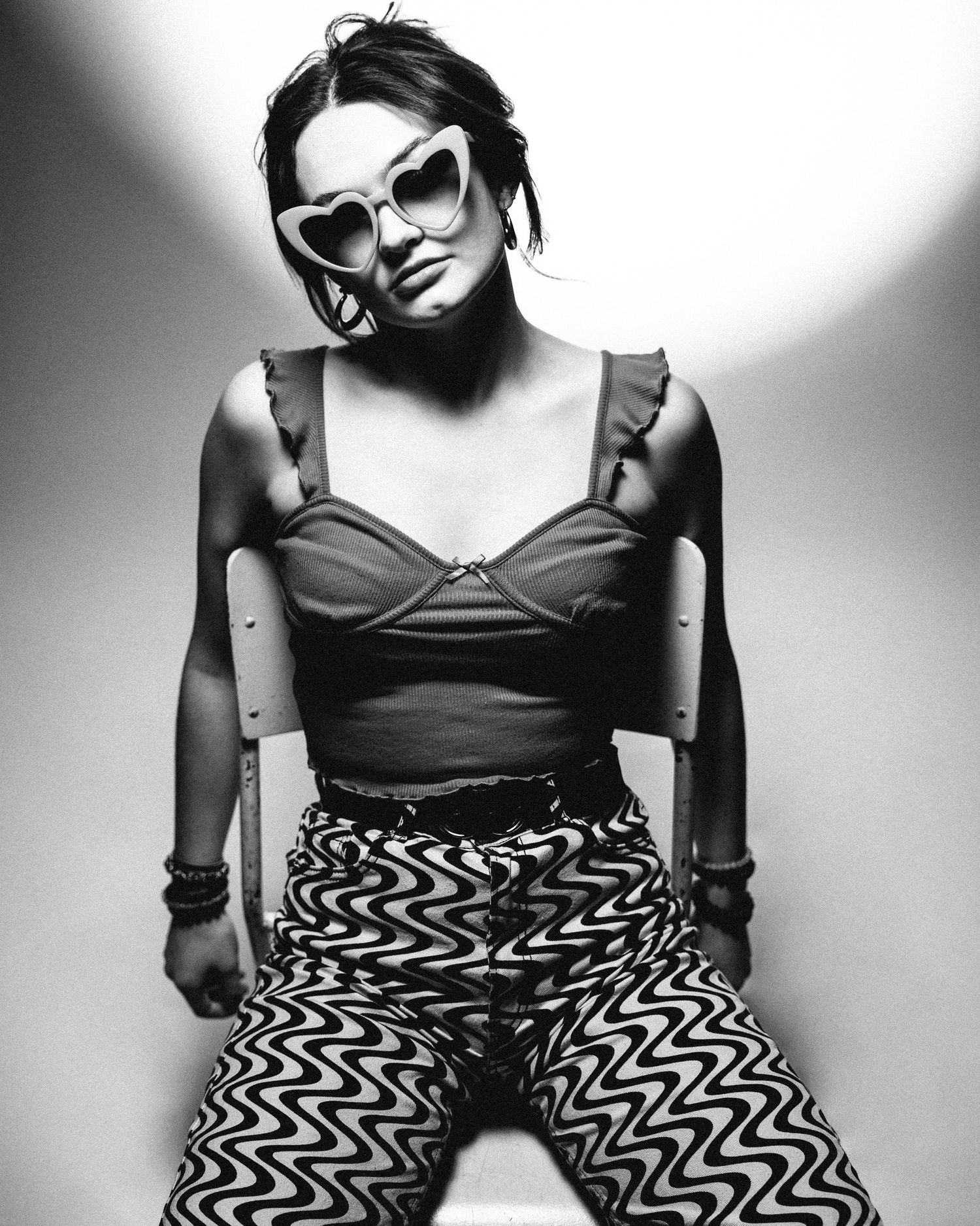 Black and white portrait of a person wearing sunglasses and geometric patterned pants in a stylish fashion pose.