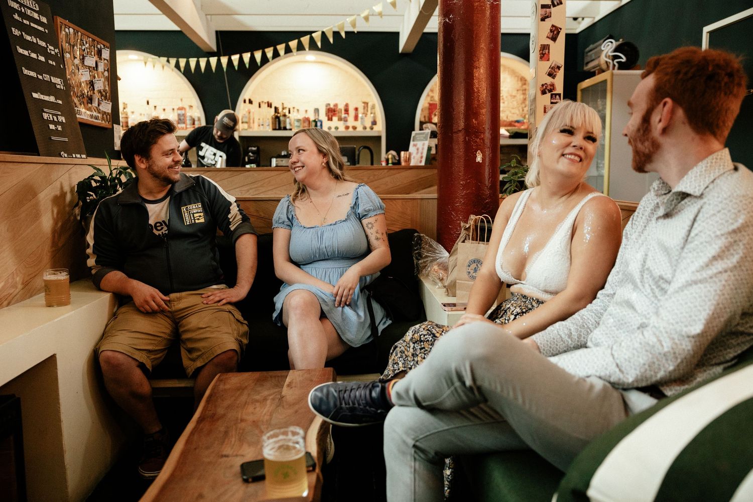 A group of friends laugh and socialize together while sitting in a pub booth with drinks.