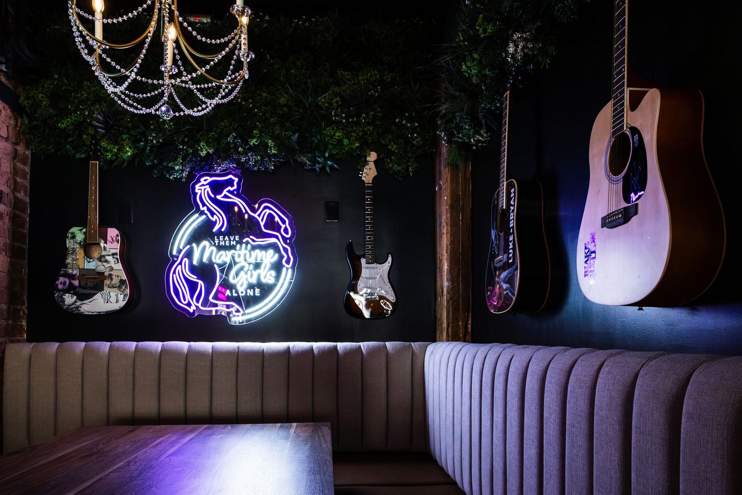 A dimly lit lounge interior with neon signs and illuminated guitars mounted on the wall above curved booth seating.