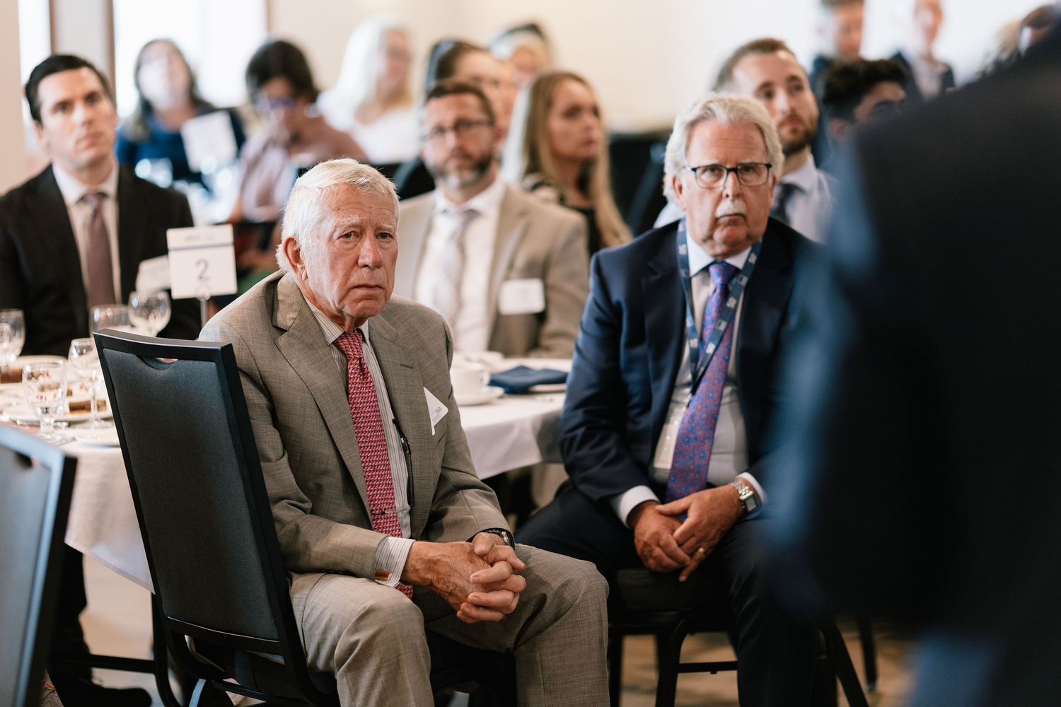 Business professionals seated in rows at a corporate conference or meeting in a bright indoor venue.