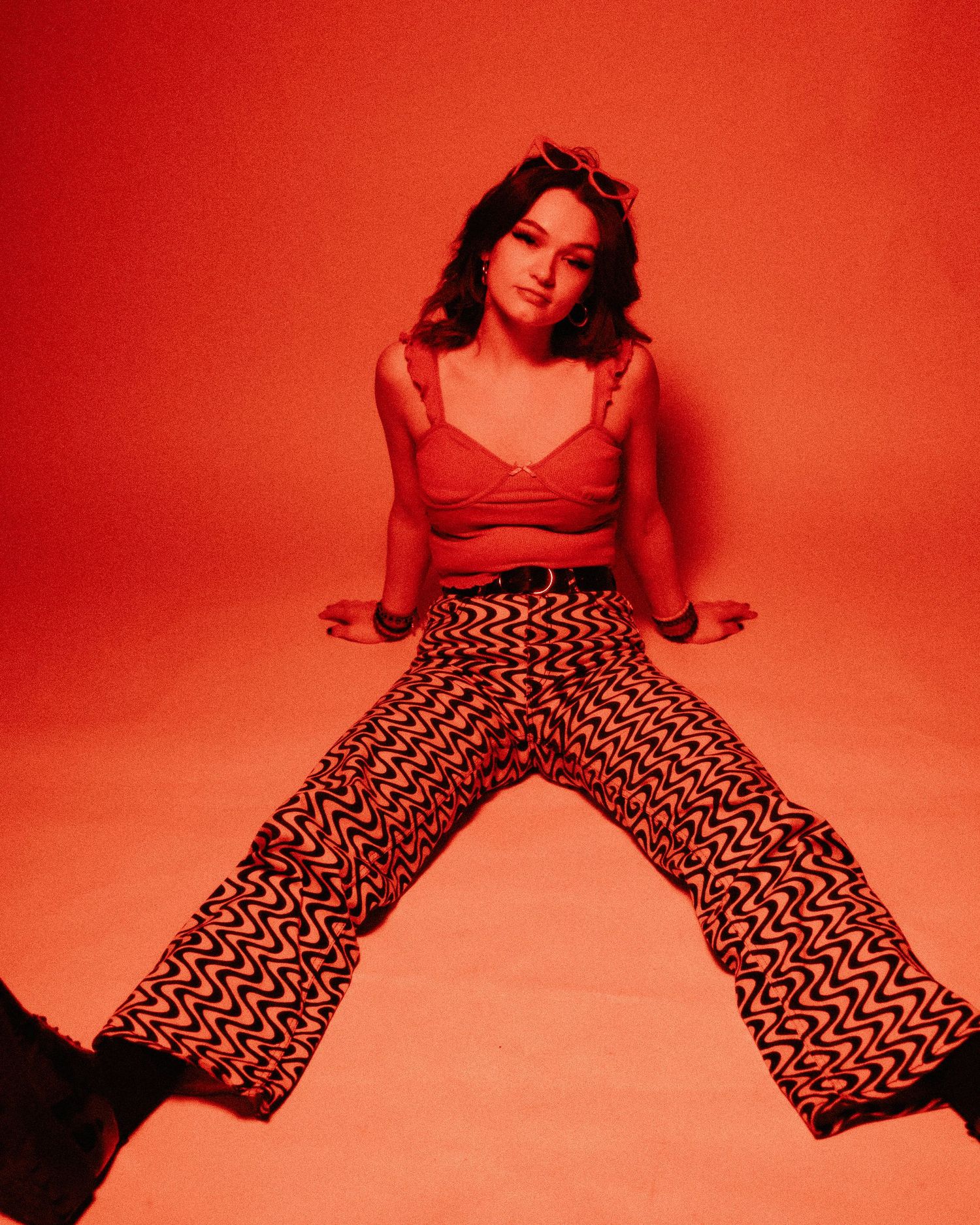 A fashion portrait against a red backdrop features someone in wide-leg patterned pants and a red top.