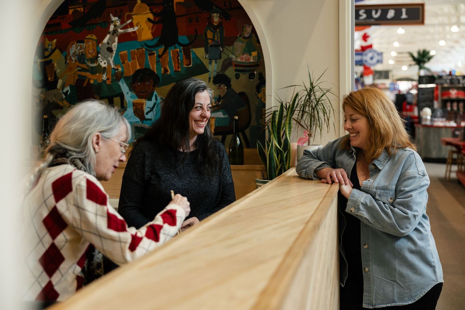 Three people engage in animated conversation while seated at a wooden counter in a casual setting.