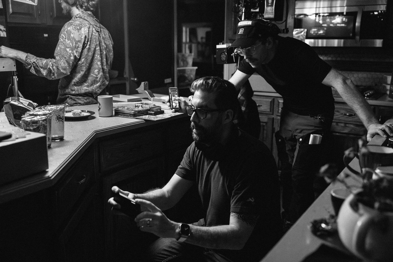 A person sits at a dimly lit counter while working with various items and equipment in a black and white photograph.