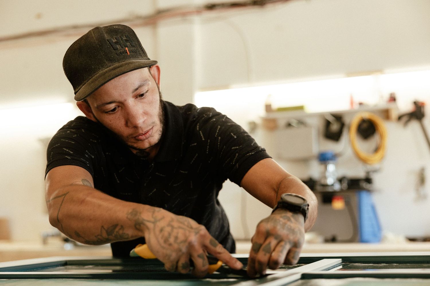 Craftsperson wearing a black hat works meticulously on a flat surface in a workshop setting.