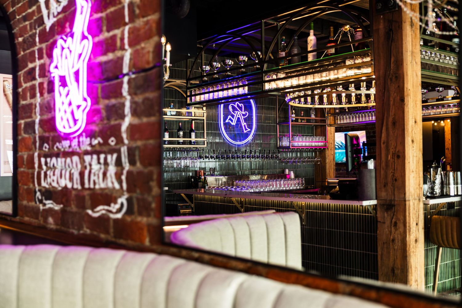 Modern bar interior with neon signs, leather booth seating, and exposed brick walls showcasing a vibrant nightlife atmosphere.