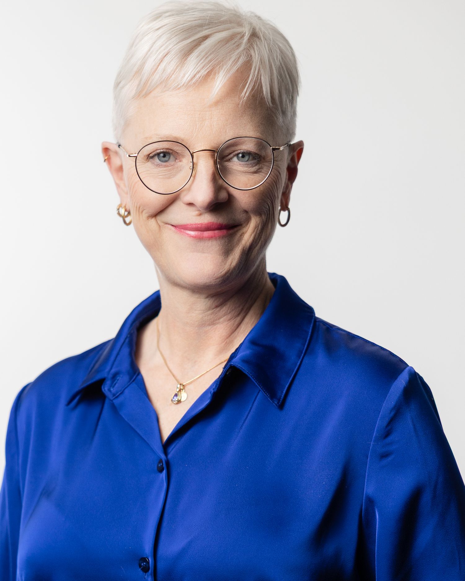 Professional headshot portrait of someone wearing glasses and a bright royal blue blouse against a light background.